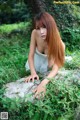 A woman in a white dress sitting on a rock in the grass.