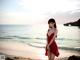 A woman in a red dress standing on a beach.