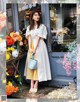 A woman standing in front of a flower shop holding a blue bag.