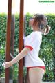 A woman in a white shirt and red panties leaning against a fence.