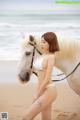 A woman in a white bikini standing next to a white horse.