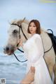 A woman in a white dress standing next to a white horse.