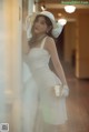 A woman in a white dress and hat leaning against a wall.