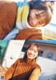 A young girl wearing a brown sweater and a yellow and blue blanket.