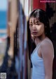 A woman in a white tank top leaning against a wall.