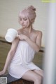 A woman in a white towel sitting in a bathtub holding a cup.