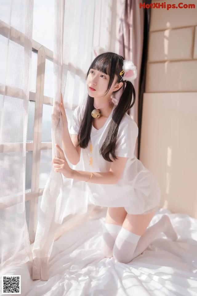 A woman in a white dress is sitting on a bed.