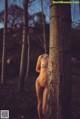 A naked woman standing next to a tree in the woods.