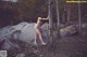 A naked woman standing on a rock in the woods.