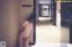 A naked woman leaning against a wall in a hallway.