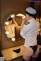 A woman in a white shirt and black panties is looking at herself in the mirror.