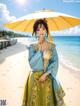 A woman in a blue and yellow dress holding an umbrella on the beach.