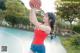 A woman in a red shirt and blue shorts holding a basketball.